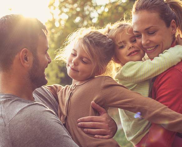 Liebevoll kuschelnde Familie in der Sonne im Wald